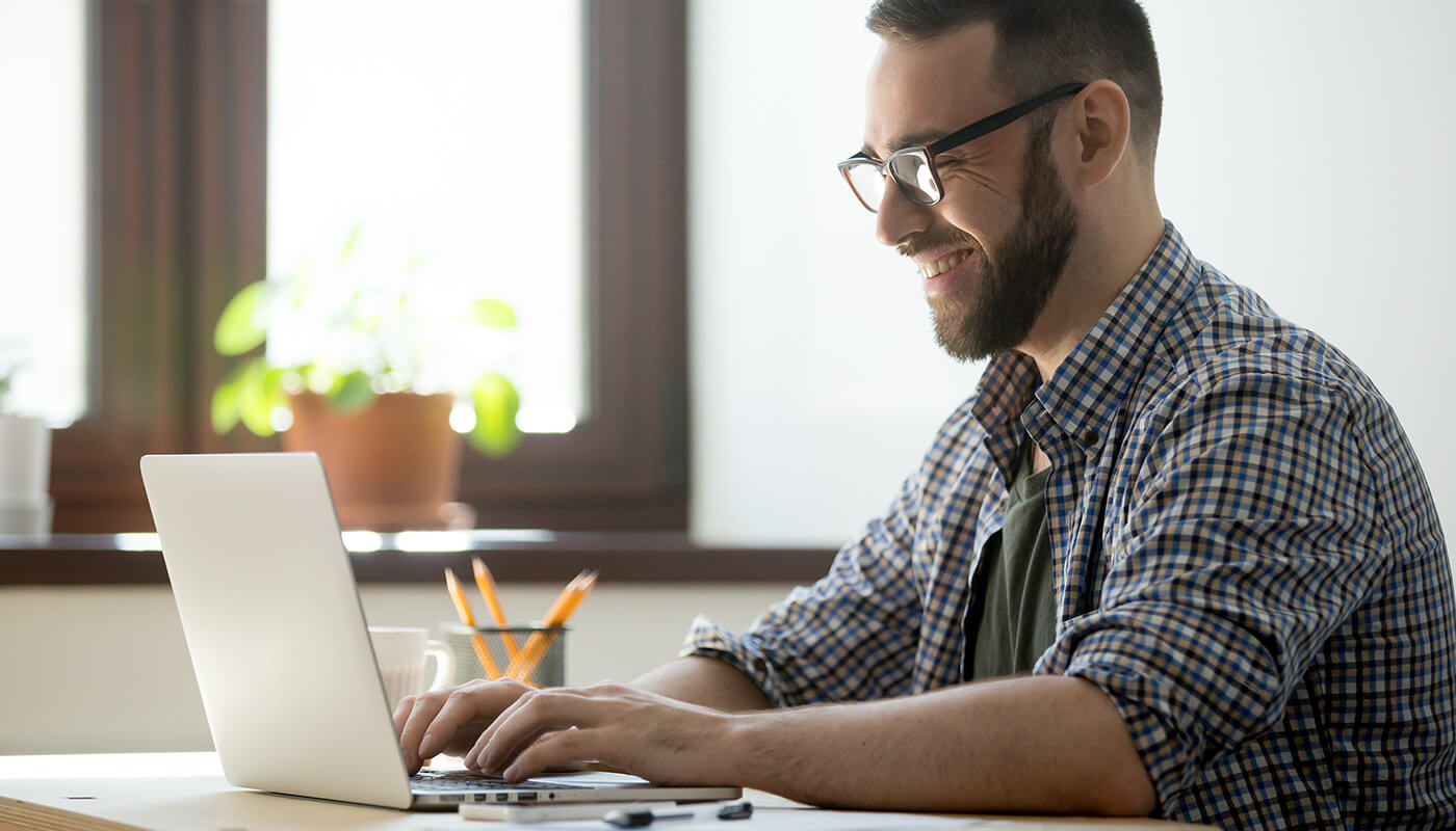 man with a smile typing on his laptop