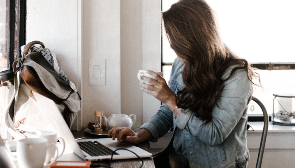 woman using her computer while drinking coffee